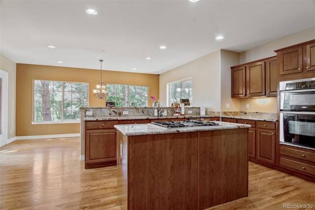 kitchen with light stone counters, decorative light fixtures, appliances with stainless steel finishes, kitchen peninsula, and light hardwood / wood-style floors