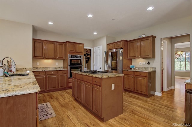 kitchen with sink, light stone countertops, light hardwood / wood-style floors, and appliances with stainless steel finishes