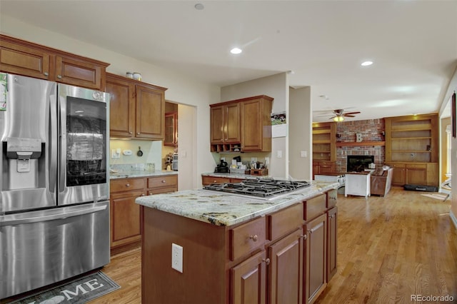 kitchen with light hardwood / wood-style flooring, ceiling fan, appliances with stainless steel finishes, a kitchen island, and a brick fireplace