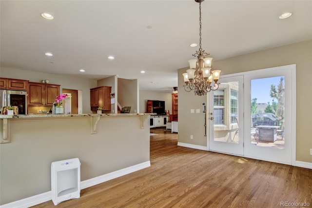 kitchen featuring a breakfast bar, decorative light fixtures, stainless steel refrigerator, light stone countertops, and light hardwood / wood-style floors