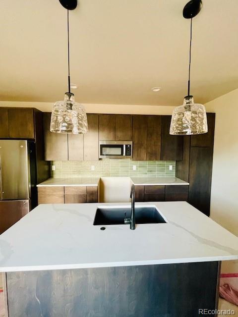 kitchen with decorative backsplash, stainless steel appliances, a sink, and hanging light fixtures