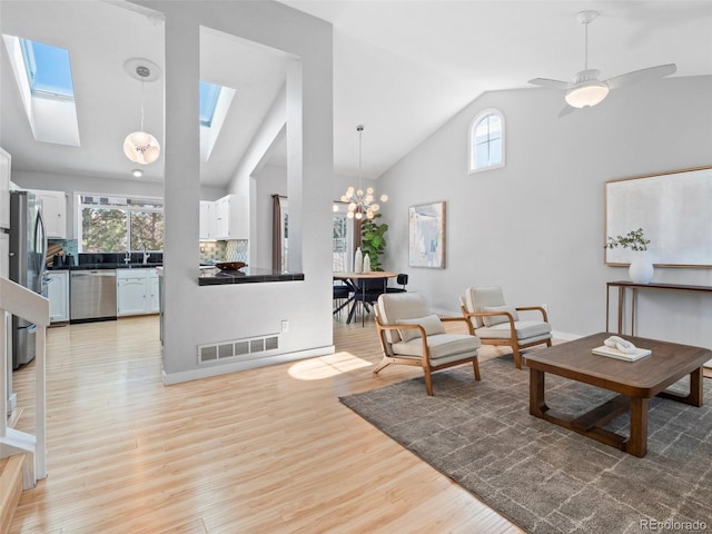 living area featuring a skylight, visible vents, light wood finished floors, and high vaulted ceiling