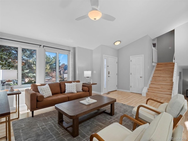 living area with a ceiling fan, vaulted ceiling, wood finished floors, baseboards, and stairs