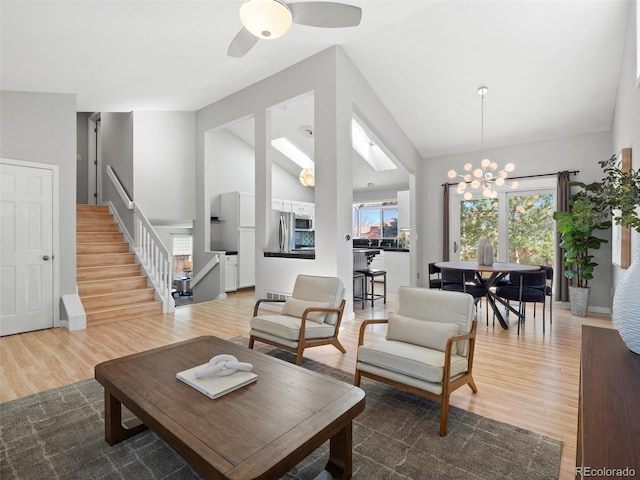 living area featuring stairs, high vaulted ceiling, ceiling fan with notable chandelier, and wood finished floors