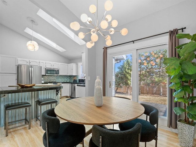 dining room featuring a chandelier, vaulted ceiling with skylight, and light wood finished floors