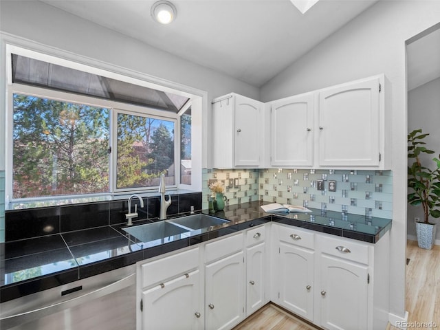 kitchen featuring decorative backsplash, stainless steel dishwasher, white cabinets, vaulted ceiling, and a sink