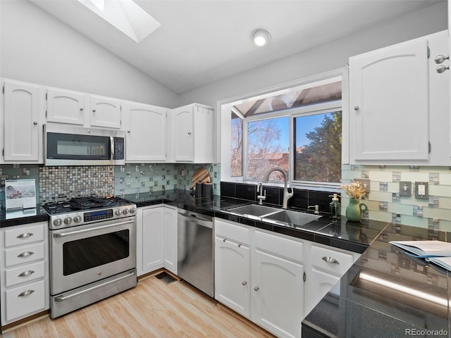 kitchen with white cabinets, lofted ceiling with skylight, stainless steel appliances, light wood-type flooring, and a sink