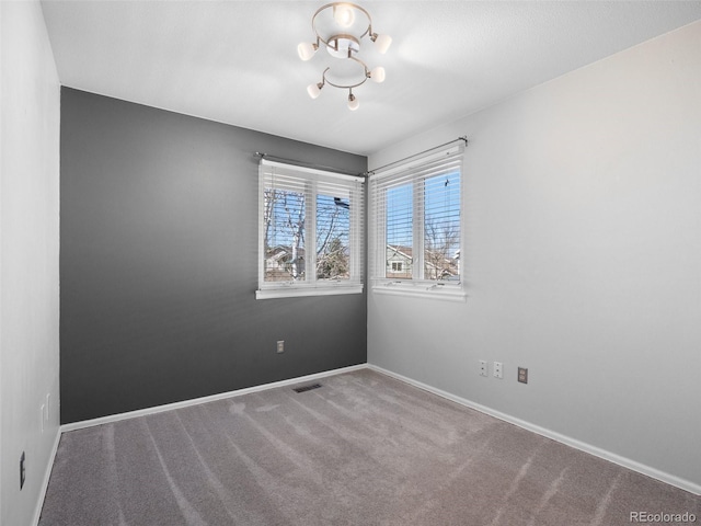 carpeted empty room featuring visible vents, baseboards, and a notable chandelier