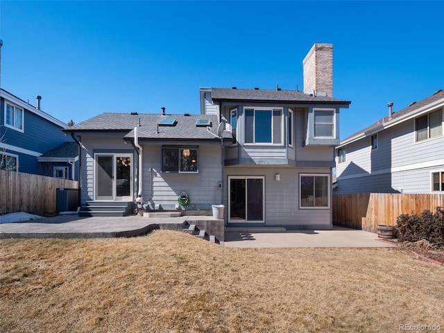 back of property with entry steps, a patio, a fenced backyard, a chimney, and a yard