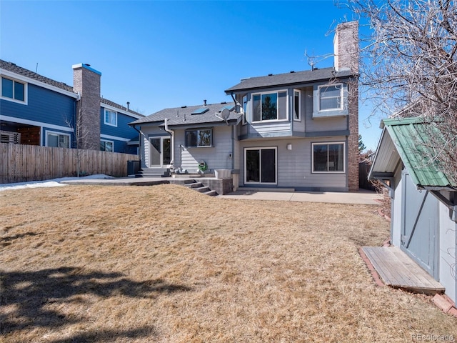 rear view of property with entry steps, a lawn, a patio, a chimney, and fence