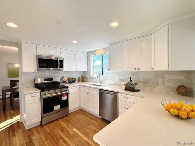 kitchen with appliances with stainless steel finishes, light wood-type flooring, backsplash, sink, and white cabinets