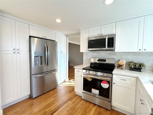 kitchen with decorative backsplash, white cabinetry, stainless steel appliances, and light hardwood / wood-style floors