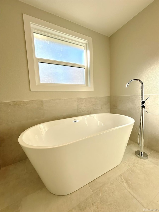 bathroom with tile patterned flooring, a bath, and tile walls