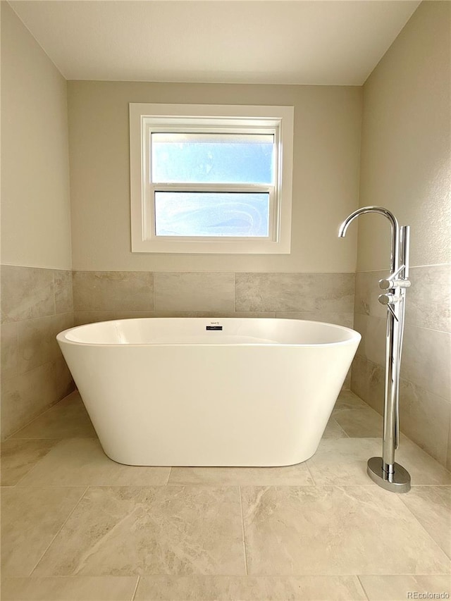 bathroom featuring tile patterned flooring, a tub to relax in, and tile walls