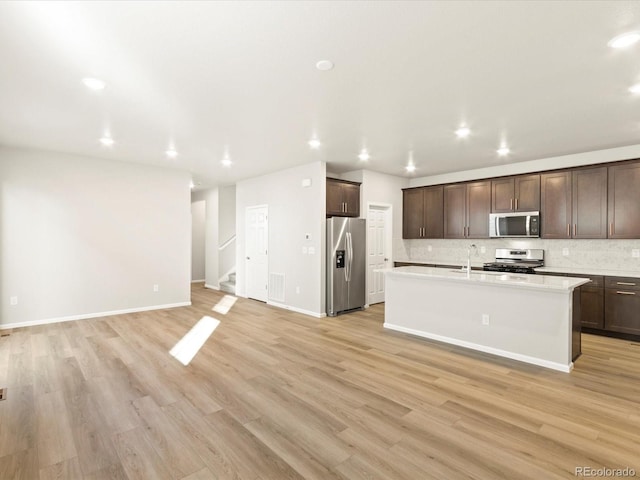 kitchen featuring a kitchen island with sink, dark brown cabinets, stainless steel appliances, and light hardwood / wood-style floors