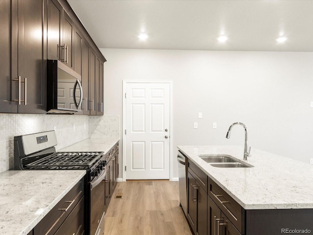 kitchen with a kitchen island with sink, sink, light hardwood / wood-style flooring, light stone countertops, and appliances with stainless steel finishes