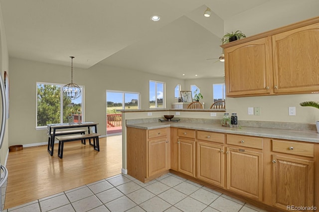 kitchen featuring kitchen peninsula, light wood-type flooring, ceiling fan with notable chandelier, and hanging light fixtures