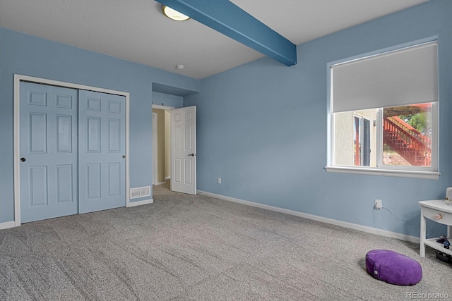 unfurnished bedroom featuring carpet flooring, a closet, and beamed ceiling