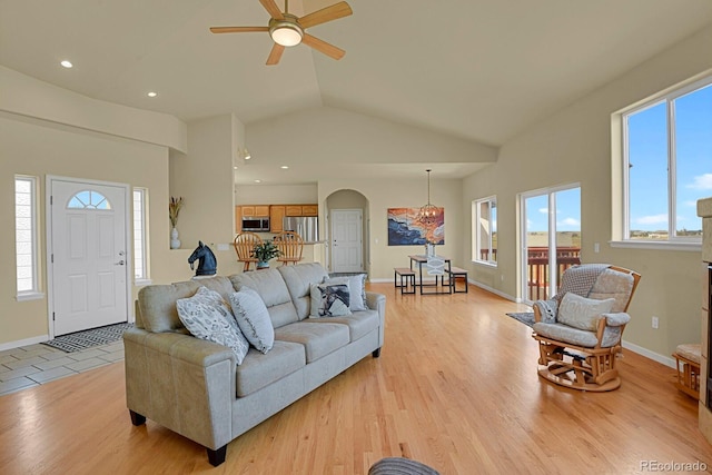 living room featuring high vaulted ceiling, ceiling fan with notable chandelier, and light hardwood / wood-style floors