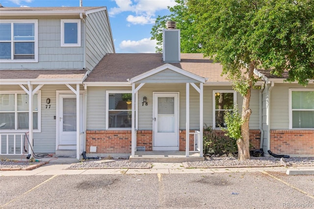 8260 Washington St Unit 78, Denver, CO 80229 - view of front of house with brick siding, a chimney, a shingled roof, and covered porch