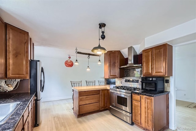 4934 S Flower Way, Littleton, CO 80123 - kitchen featuring wall chimney range hood, stainless steel appliances, a peninsula, backsplash, and light wood-style floors