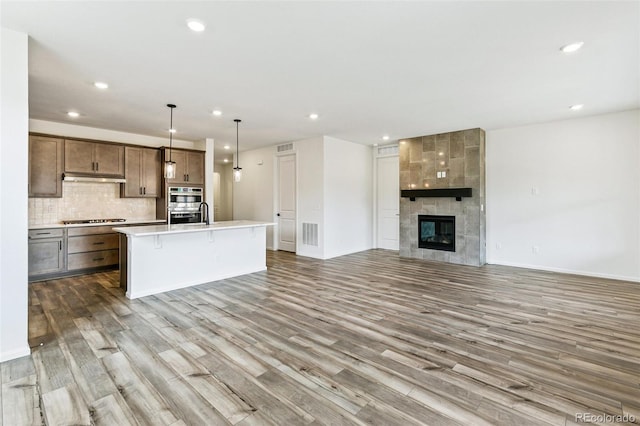 kitchen featuring appliances with stainless steel finishes, an island with sink, hardwood / wood-style floors, and hanging light fixtures