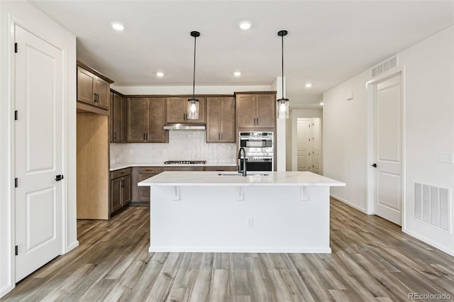 kitchen featuring stainless steel appliances, light hardwood / wood-style flooring, and an island with sink