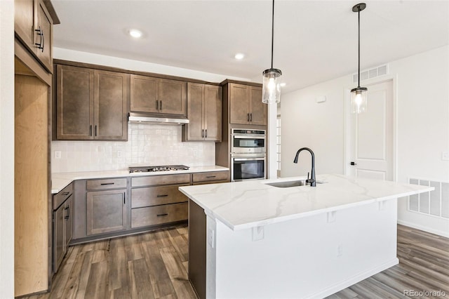 kitchen featuring sink, appliances with stainless steel finishes, an island with sink, and dark hardwood / wood-style flooring