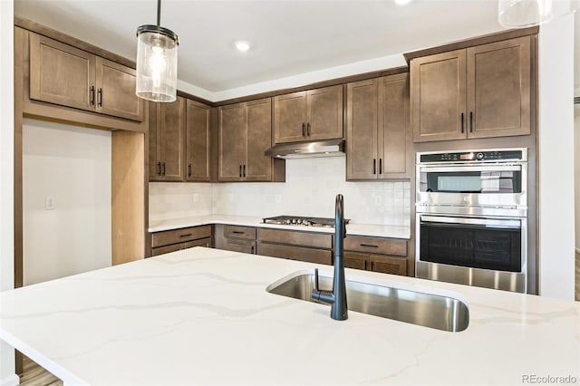 kitchen with tasteful backsplash, sink, stainless steel appliances, decorative light fixtures, and light stone counters