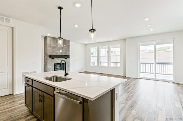 kitchen with light stone countertops, dishwasher, pendant lighting, light hardwood / wood-style floors, and sink