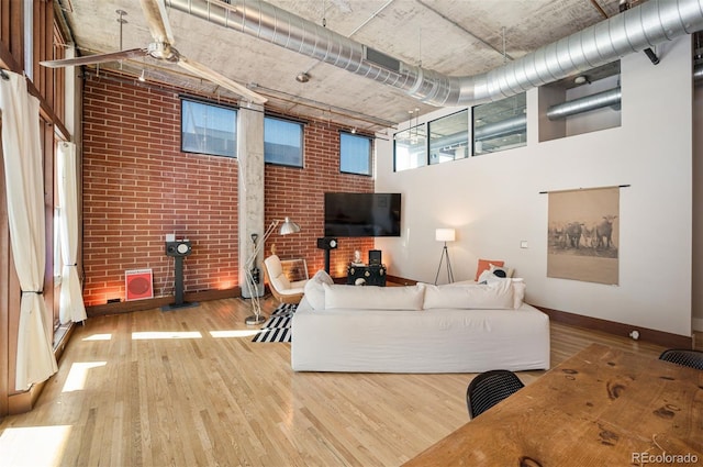 living room with a towering ceiling, brick wall, baseboards, and wood finished floors