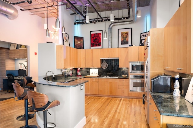 kitchen with a peninsula, appliances with stainless steel finishes, light brown cabinets, and a towering ceiling