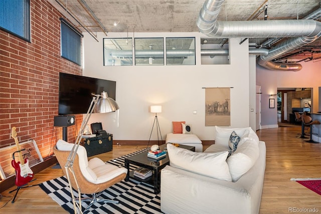 living area featuring brick wall, a high ceiling, an accent wall, wood finished floors, and baseboards