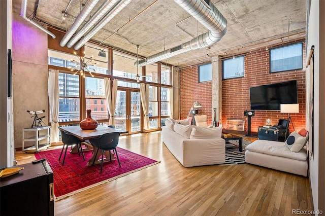 living area with a towering ceiling, brick wall, wood finished floors, expansive windows, and a notable chandelier