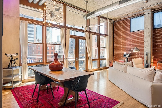 dining space featuring brick wall, a high ceiling, wood finished floors, and french doors