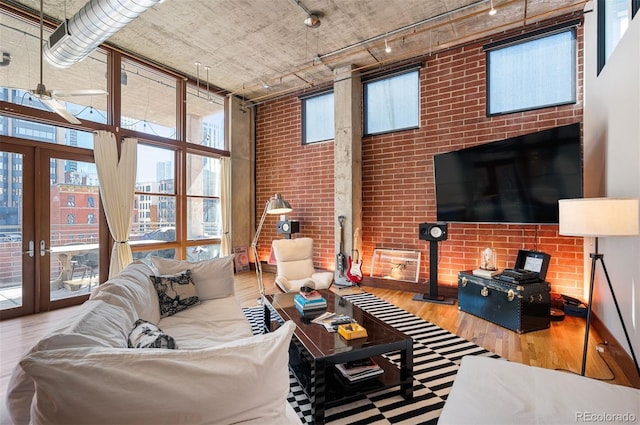 living area featuring french doors, wood finished floors, a towering ceiling, track lighting, and brick wall