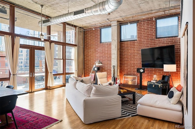 living room featuring french doors, a high ceiling, expansive windows, brick wall, and wood finished floors