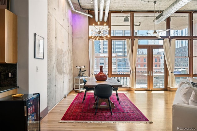 dining area featuring wine cooler, wood finished floors, an inviting chandelier, a high ceiling, and floor to ceiling windows