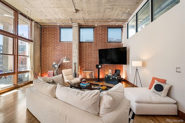 living area with brick wall, a high ceiling, and wood finished floors