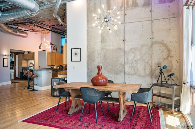 dining space with an inviting chandelier, a high ceiling, baseboards, and wood finished floors