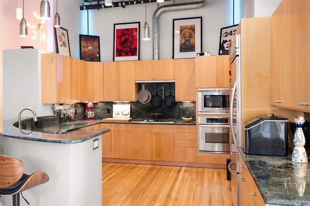 kitchen with a peninsula, appliances with stainless steel finishes, light brown cabinetry, and tasteful backsplash