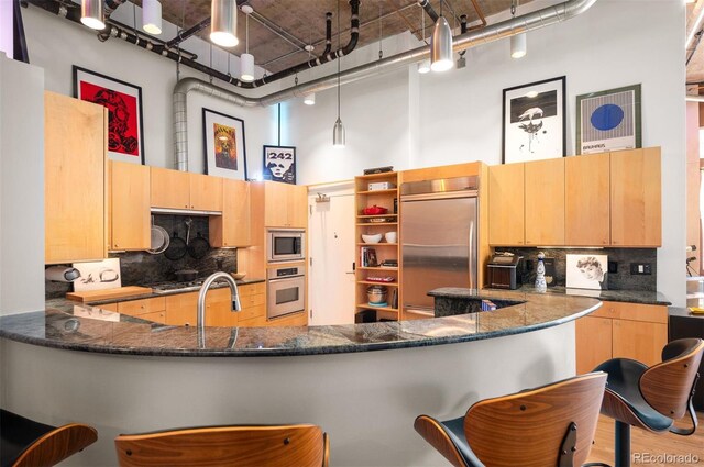 kitchen featuring built in appliances, a high ceiling, light brown cabinets, and tasteful backsplash