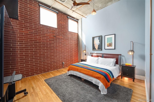 bedroom featuring brick wall, wood finished floors, and a towering ceiling