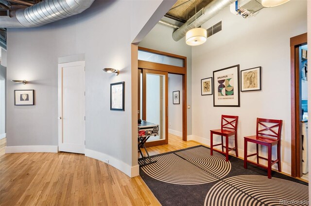 corridor with visible vents, a towering ceiling, baseboards, and wood finished floors