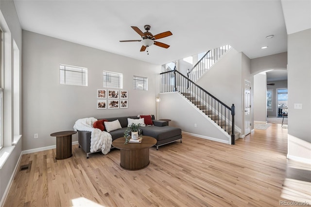 living room featuring arched walkways, visible vents, baseboards, stairway, and light wood finished floors