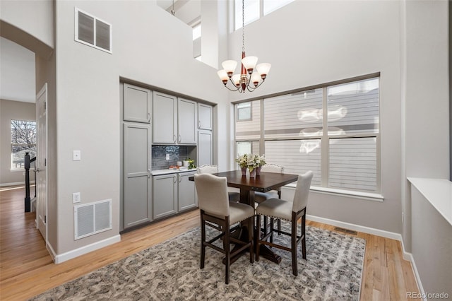 dining space with baseboards, light wood-type flooring, visible vents, and a notable chandelier