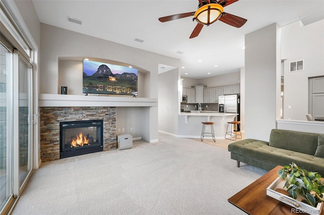 living room featuring recessed lighting, visible vents, light colored carpet, and a stone fireplace