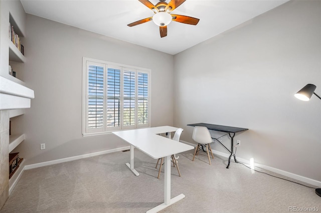 office space featuring baseboards, a fireplace, a ceiling fan, and light colored carpet