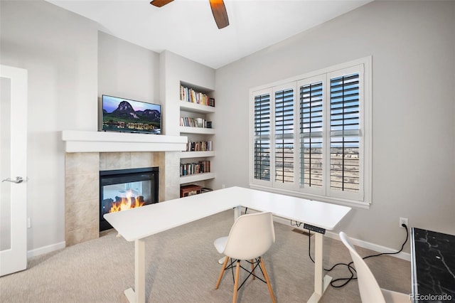 home office with baseboards, built in shelves, a fireplace, and light colored carpet