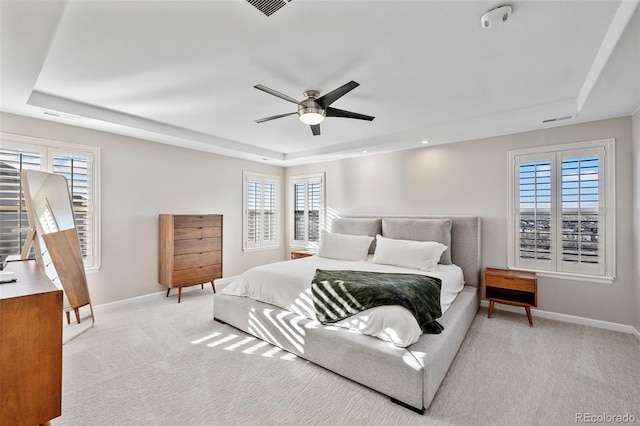 bedroom with a tray ceiling, light carpet, and baseboards